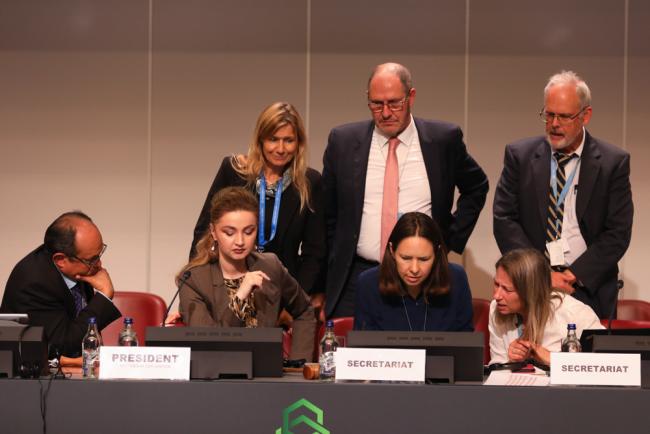 Members of the BRS Secretariat huddle on the podium as discussions about the proposed amendment to the Rotterdam Convention are discussed