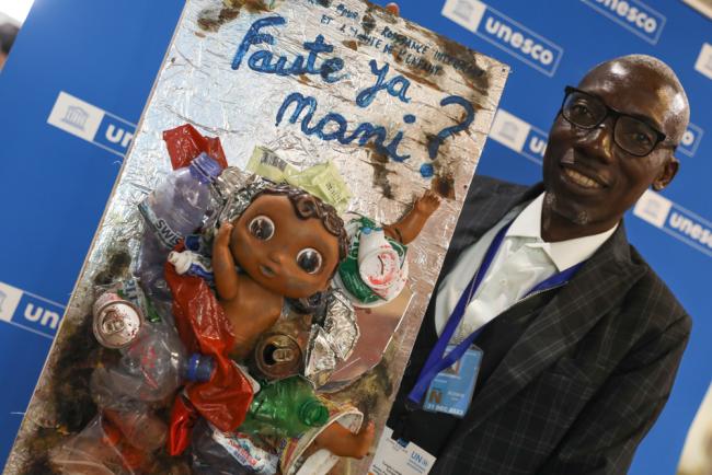 Adolphe Tungilu Luwana, Office for the Integrated Growth and the Dignity of the Child (BCIDE), holds a piece of art made by children in the Democratic Republic of the Congo that asks 'who's fault is this?'