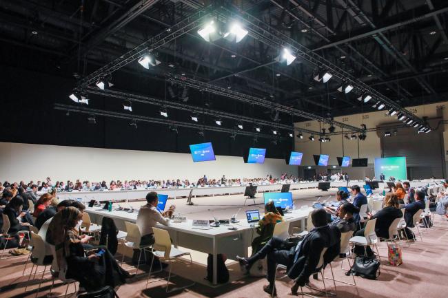 View of the room during informal negotiations on the Delegates negotiating in a huddle during informal consultations on the Warsaw International Mechanism for Loss and Damage