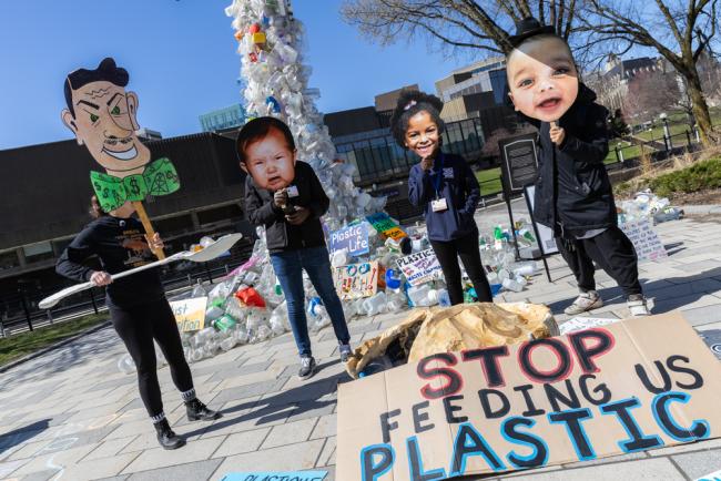 Members of civil society demonstrate outside the venue, showing how plastic producers are 'feeding' plastics to society