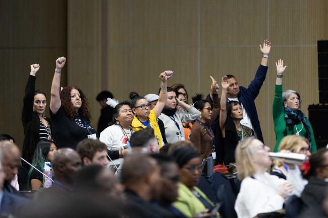 During the stocktaking plenary, members of civil society stand and raise their fists, calling for the INC-5 Chair to give rights holders an opportunity to speak