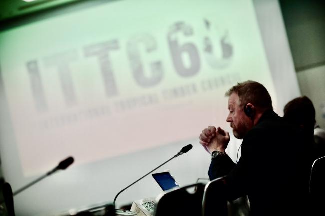A conference scene with "ITTC60" displayed; the man is holding his hands and listening via headphones.
