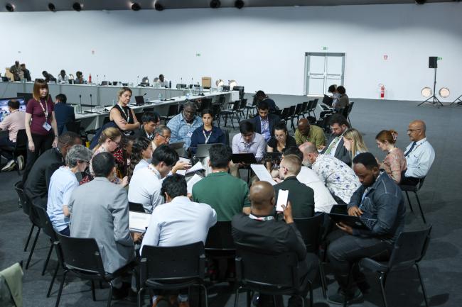Delegates forming a huddle during informal consultations on the framework for non-market approaches under the Paris Agreement